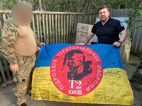 Двоє людей тримають прапор поруч із коробками.